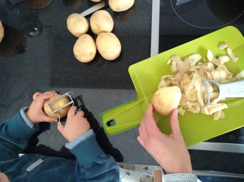 Kind hilft Kartoffeln schälen